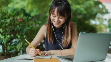 happy young asian student doing homework and listening to music with earphones